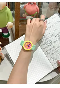Detailed shot of a cute cartoon watch with a yellow bezel and green silicone strap on a wrist.
