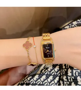 Close-up of Dinimi gold steel quartz watch with black dial and clover charm bracelets