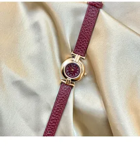 Close-up detail of a vintage red leather strap watch presented on gold silk background