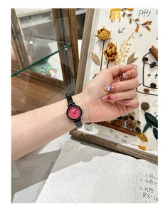 Close-up of a cute small round watch with a red dial and black strap on an Asian wrist.