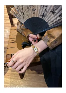 Nahaufnahme einer goldenen Vintage-Quarzuhr am Handgelenk mit einem Faltfächer-Hintergrund.