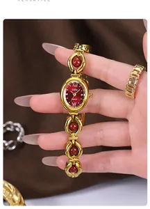 Detailed view of an elegant gold bracelet watch with red beads and a vintage oval dial