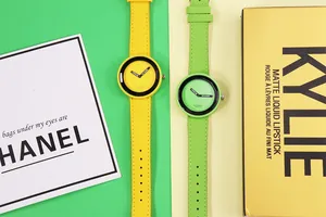 Orologi al quarzo minimalisti giallo e verde con accessori moda su sfondo bicolore.