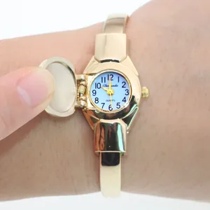 Close-up of a gold-tone flip-cover bangle watch with a light blue dial on wrist