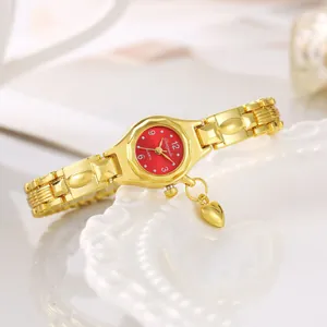 Dettaglio elegante di orologio a bracciale dorato con quadrante rosso e ciondolo.