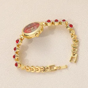 Close-up of luxury gold-toned bracelet watch featuring red gemstones and crystal accents