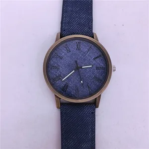 Close-up of a denim-textured quartz watch with a vintage bronze case and Roman numerals.