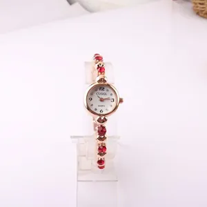 Close-up detail of a rose gold women's quartz watch featuring a red rhinestone bracelet