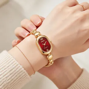 Close-up detail of a luxury gold bean link bracelet watch with an oval red dial