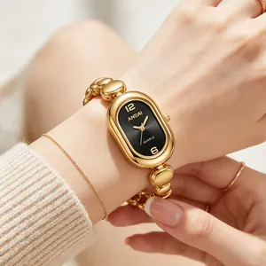 Close-up of an elegant gold bean link oval watch with a black dial on a woman's wrist