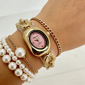 Gros plan d'une élégante montre ovale dorée avec cadran rose et bracelets en perles