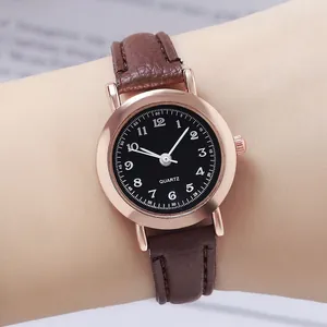 Gros plan d'une montre noire minimaliste avec bracelet fin en cuir marron au poignet.