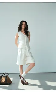 Full length view of a woman wearing a white knit vest and shorts in a minimalist setting.