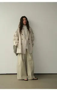 Mannequin portant un trench-coat croisé beige minimaliste dans un studio de photographie.