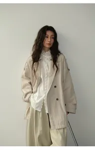 Vue détaillée d'un trench-coat beige porté avec un chemisier blanc à volants