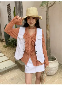 Gilet en jean blanc rétro avec surpiqûres contrastées porté sur un chemisier orange à volants