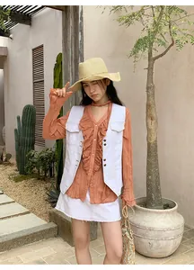 Gilet en jean blanc à surpiqûres contrastées porté avec un chemisier à volants orange