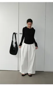 Full length view of elegant white wide-leg trousers styled with a black ruffled top.