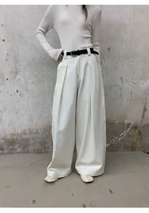 Femme portant un pantalon large blanc en jean avec une ceinture noire sur béton