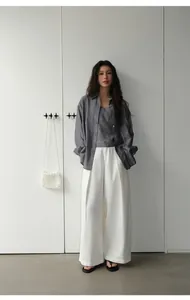 Model wearing retro white wide-leg denim trousers and a grey shirt in a minimalist room