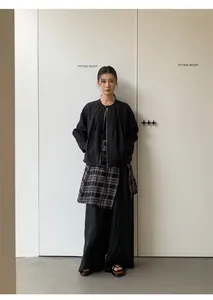 Schicke asiatische Frau trägt weite schwarze Hosen und eine Faltenjacke in der Umkleidekabine