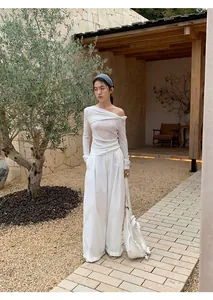 Asian model in white off-shoulder top and wide-leg trousers in a minimalist garden