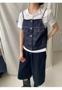 Dettaglio di un gilet a canotta in denim scuro sovrapposto a una maglietta bianca su una modella