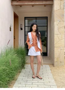 Vue détaillée d'une femme portant un gilet en jean blanc sur un chemisier orange à volants.