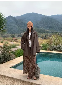 Femme élégante en trench-coat marron mi-long à double boutonnage dehors près d'une piscine