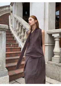 Elegant woman in brown sleeveless top and irregular pleated skirt on stone stairs