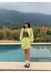 Outdoor lifestyle-foto van een vrouw in een limoengroene rok met trekkoord en jas bij een zwembad