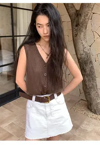 Close-up detail of a brown knitted mesh vest styled with a white skirt and brown leather belt