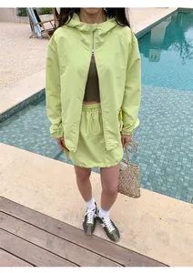 Vrouw in lindegroen outdoor jack met capuchon en bijpassende mini-rok met trekkoord