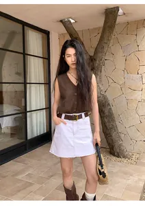 Stylish Asian woman posing in a brown knit vest and white denim skirt outdoors