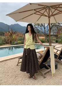 Detail of a pale yellow knit vest paired with a plaid maxi skirt by a relaxing pool