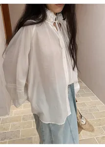 Detail of a light blue straight denim midi skirt styled with a white ruffled shirt.