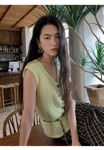 Close-up of a pale yellow washi silk mesh knit vest worn by an Asian model in a cafe setting.