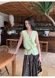 Close-up of a pale green V-neck knit vest featuring mesh splicing in a cafe setting