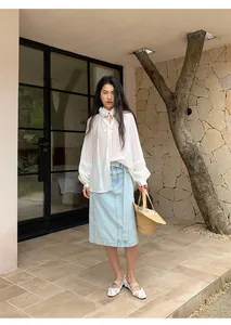 Detailed shot of light blue straight denim skirt paired with a white bohemian blouse.