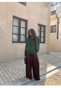 Elegant woman in green knit sweater and brown wide-leg pants posing on European street