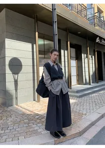Model poseert in stad met stijlvolle zwarte broek met wijde pijpen en grijs vest