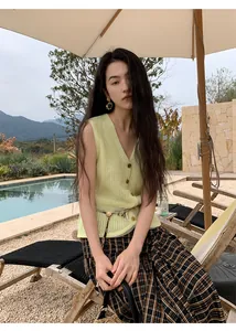 Young woman wearing a light yellow knitted mesh vest sitting by a scenic resort swimming pool