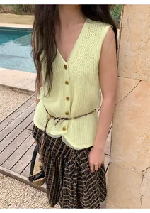 Detail of light yellow knit vest featuring mesh layering and button-down V-neck design.
