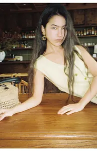 Detail shot of a woman in a light yellow knitted vest leaning on a rustic wooden table