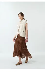 Full look of a woman wearing a brown 3D pleated bias cut midi skirt with cream vest.