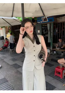 Detailed view of a minimalist beige cotton vest and wide-leg pants set on model at a cafe