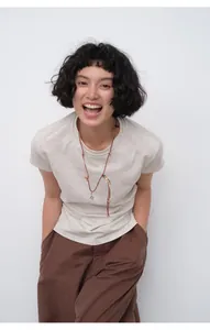 Model wearing a slim fit beige short sleeve T-shirt with gathered waist detail and necklace.