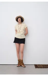 Full body view of woman in slim fit pleated waist cream T-shirt and black mini skirt