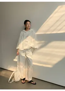 Full body view of a woman wearing a white oversized hooded sweatshirt and wide-leg pants.