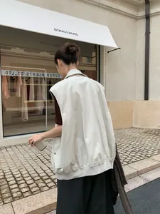 Back view of a woman wearing an oversized white PU leather vest in a street style setting